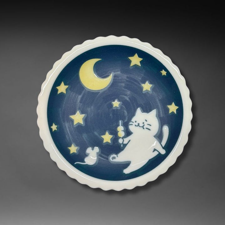 An overhead view of the full 14.1 cm scalloped plate. The design features a white cat holding dango, a mouse, a crescent moon, and stars on a deep blue night sky background.