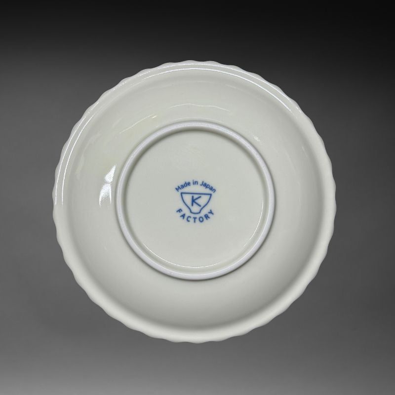 An inverted view of the underside of the ceramic plate, showing the white base and the blue K Factory 'Made in Japan' mark stamped in the centre of the foot.