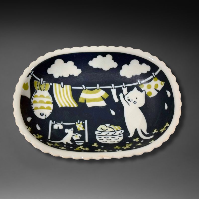 An overhead view of the full oval ceramic bowl. The design features a white cat and mouse hanging laundry on a line under white clouds, set against a dark blue background.