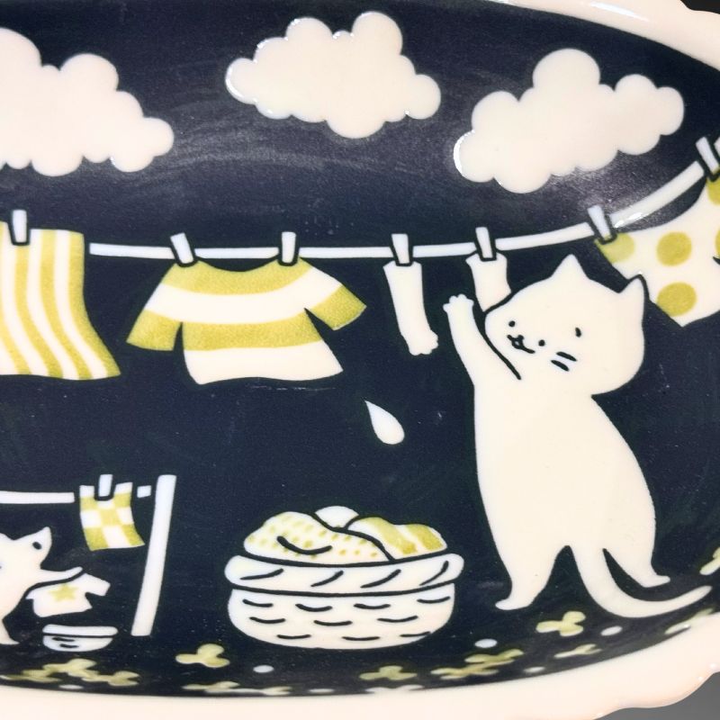 A close-up detail shot of the oval bowl's interior, showing the smiling white cat, a laundry basket, and clothes pegged on the line.