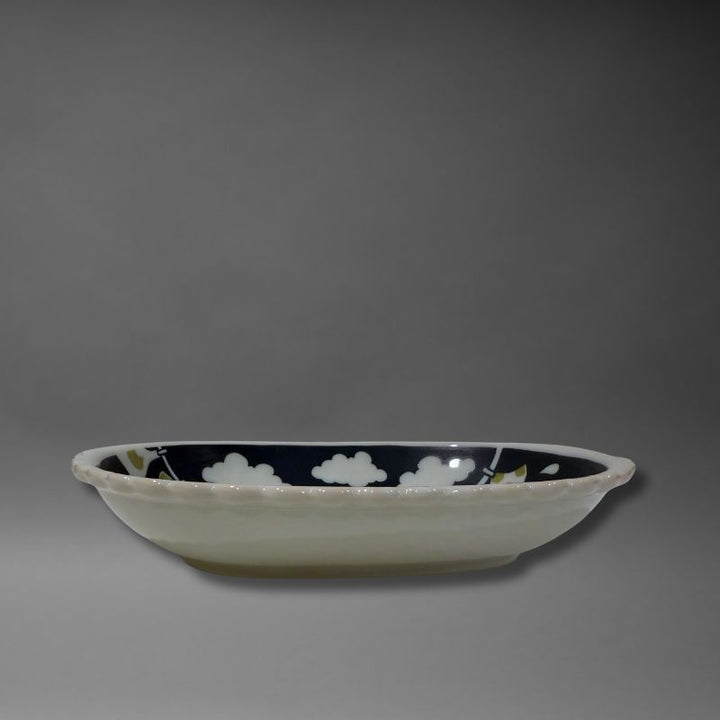 A low-angle side view of the oval serving bowl, highlighting its depth and the white, scalloped 'biscuit' rim and exterior. The interior design is partially visible.