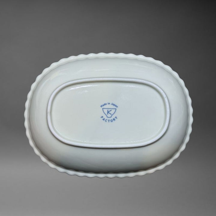 An inverted, bottom-up view of the oval ceramic bowl, clearly showing the white base and the blue K Factory 'Made in Japan' mark stamped in the centre.