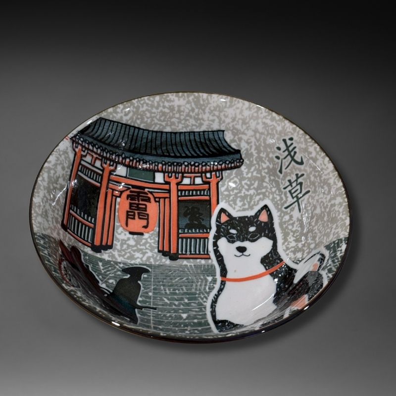 A studio shot of the ramen bowl's interior, featuring a black and white Shiba dog in front of the iconic red and black Kaminarimon Gate of Asakusa, with the Japanese text '浅草' (Asakusa) visible.