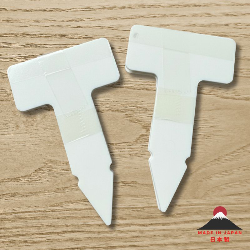 Two T-shape white polypropylene plant name tags on a wooden surface, pointed stakes visible, size 49×79 mm, Made in Japan.