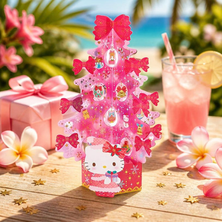 Sanrio Hello Kitty pink Christmas tree card on an outdoor table with frangipani, pink lemonade and a beach behind, Australian summer Christmas