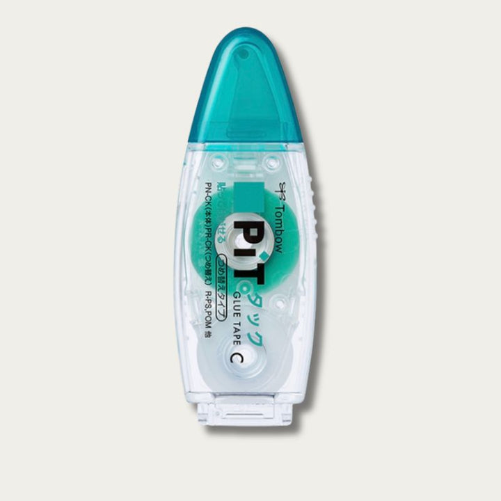 Front view of the Tombow PiT Tack-C glue tape dispenser. Features a compact, clear oval body with a teal internal tape reel and a matching teal protective cap.