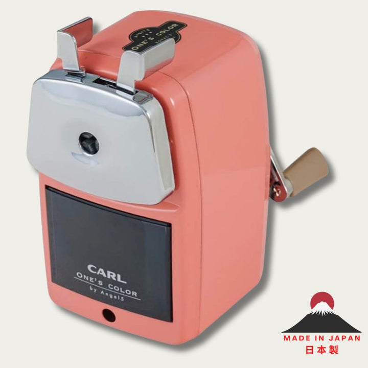 Front view of the CARL Angel 5 Royal 3 manual pencil sharpener in pink with a chrome faceplate, dark translucent shavings receptacle, and a "Made in Japan" logo in the bottom corner.