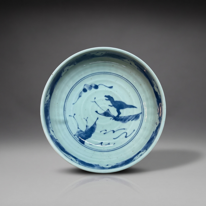 shinogi-medium-bowl-mino-ware.jpg	Edokko Dinosaur shinogi medium bowl 15.5cm in celadon glaze with blue T-rex riding a leaf over waves and a scroll pattern rim band, Mino ware made in Japan