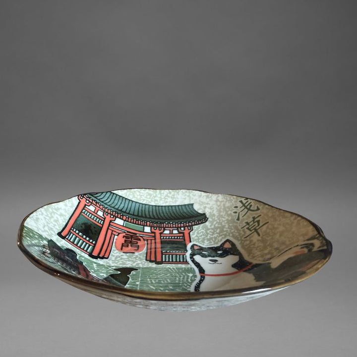 A low-angle studio view of the deep serving plate, highlighting the full design: the Shiba dog, the Kaminarimon Gate, and a silhouette of a rickshaw on the speckled grey and green interior.